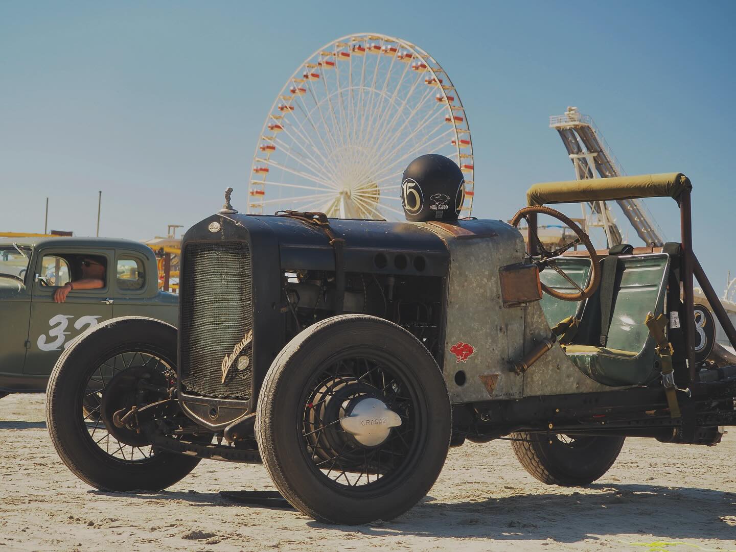 Vintage black Ford hot rod on the beach with a Ferris wheel in the background